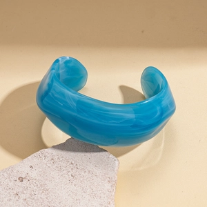 Detailed view of thick teal marble texture acrylic cuff bracelet on a stone pedestal