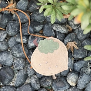 Detail of acorn-shaped leather crossbody bag with green leaf accent on grey pebbles