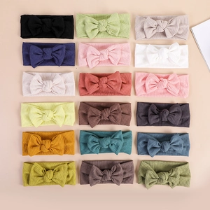 Flat lay showing eighteen assorted colors of soft ribbed baby bow headbands for girls