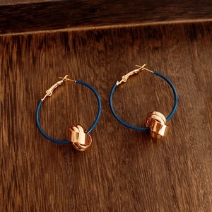 Detail of 18K gold-plated twisted knot pendant earrings on a textured wooden background