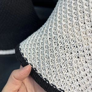 Close-up of the knitted sun hat showing beige texture and black contrast edge