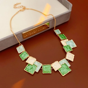 Détail du pendentif carré en émail vert et blanc sur un collier chaîne serpent dorée