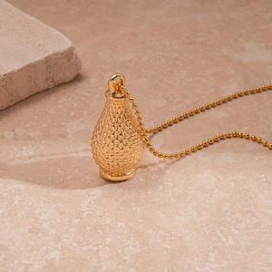 Détail d'un pendentif bouteille doré texturé avec chaîne à billes sur un fond de pierre