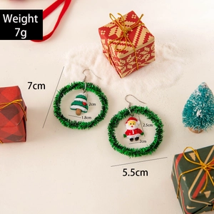 Green Christmas wreath earrings with Santa and tree charms on a festive snow background