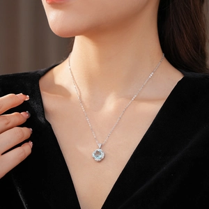 Close-up of a silver necklace featuring a light blue oval gemstone and floral pendant