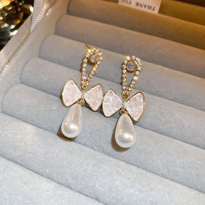 Macro detail of golden bow earrings with sparkling rhinestones and drop pearls