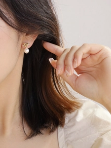 Close-up of elegant gold knot drop earring with a lustrous white pearl on model