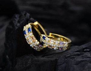 Detailed macro shot of gold hoop earrings with colorful zircon stones on dark stone