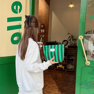 Detail of green and white striped canvas pouch held in a lifestyle cafe setting