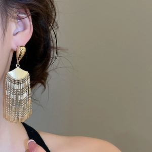Detailed close-up of a model wearing golden fan-shaped tassel earrings with metal texture