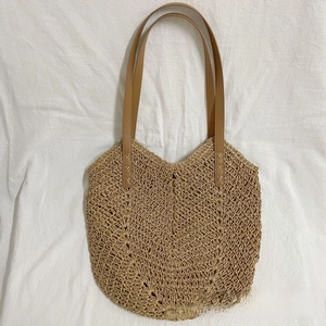 Detail of hand-woven straw tote bag featuring brown faux leather straps on white fabric