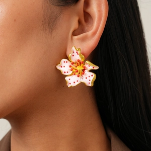 Macro detail of a pink enamel flower earring with gold outlines and red polka dots