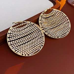 Détail de boucles d'oreilles rondes dorées avec cristaux pavés sur plateau en bois