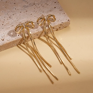 Detail of 18K gold plated bow earrings with zircon tassels on a textured stone surface