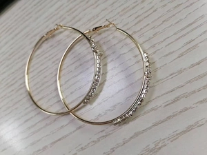 Detailed view of large golden hoop earrings with clear rhinestones on light wood