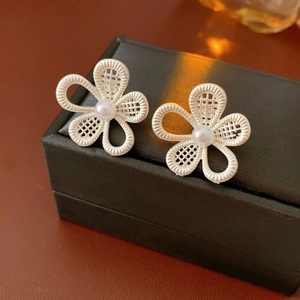 Vue macro de boucles d'oreilles fleurs argentées évidées avec perle sur une boîte
