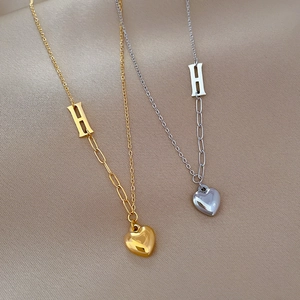 Gold and silver stainless steel H-letter heart necklaces displayed on silk fabric