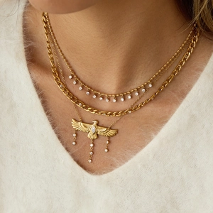 Detalle de collar multicapa con águila dorada y borlas de cristal sobre jersey blanco