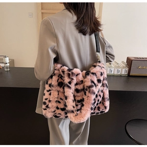 Pink plush leopard print tote bag with black adjustable strap worn by a model in a cafe