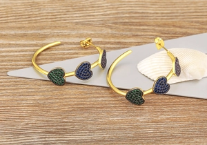 Macro detail of C-shaped 18k gold earrings featuring colorful heart-shaped zircon stones