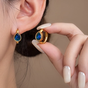 Close-up of teardrop dark blue gemstone earrings in 18K gold plated settings on model