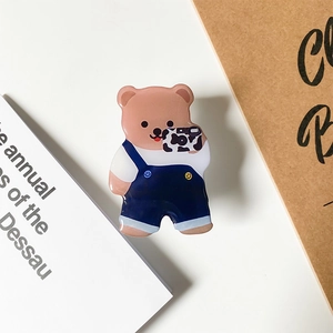 Detail of cute brown bear hair claw wearing blue overalls holding a cow print camera