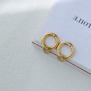 Detail of gold geometric tassel hoop earrings with fine chains on a white textured background