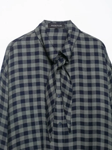 Dettaglio della camicia a quadri blu e grigio con fiocco decorativo e bottoni sul davanti