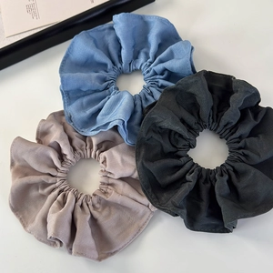 Three pleated fabric scrunchies in blue, black, and beige colors on white background