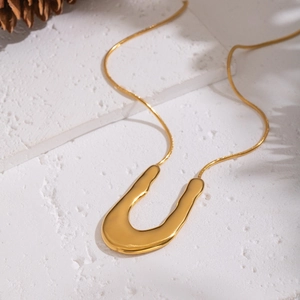 Collier maille serpent dorée avec pendentif en forme de U sur surface texturée