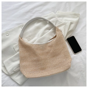 Detailed weave pattern of a beige straw shoulder bag on white fabric with fashion items