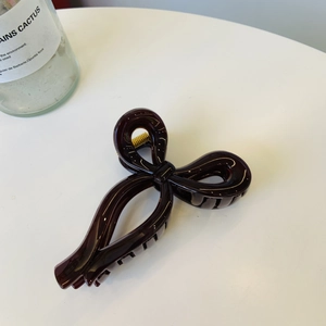 Detail of a glossy dark brown ribbon bow hair claw clip on a clean white surface
