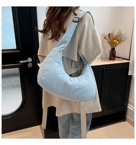 Detail of light blue quilted moon bag with wide strap on model in indoor setting