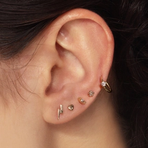 Detailed close-up of various gold S925 silver cartilage piercings and hoop earrings on ear