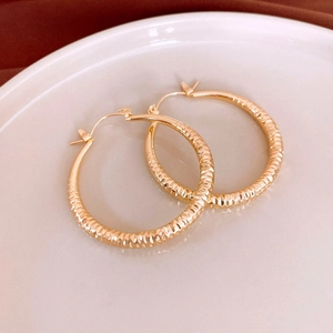Close-up of gold metal stripe hoop earrings with diamond-cut texture on white plate