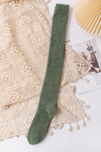 Close-up of soft green coral fleece over-knee socks displayed on delicate lace fabric