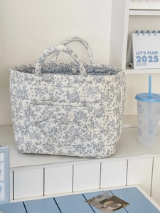 Detail of quilted corduroy floral storage basket with dual handles on a white shelf