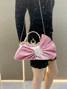 Close-up of pink pleated satin evening bag with crystal buckle and gold metal handle