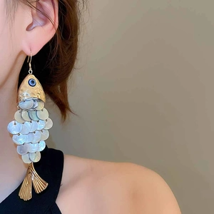Macro view of long fish-shaped earrings with seashell scales and gold metal tassels