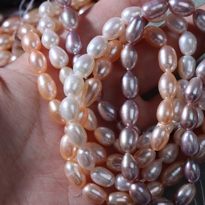 Hand holding 5-6mm natural freshwater pearls in white, pink, and purple oval shapes