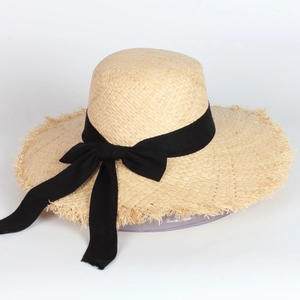 Detail of raffia sun hat featuring a wide brim with fringe edges and a black ribbon bow