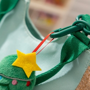 Detail view of a green fabric bag featuring a plush Christmas tree charm with yellow star