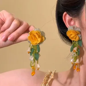 Vue détaillée de boucles d'oreilles à fleurs avec roses en tissu jaune et perles vertes