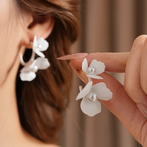 Detailed close-up of a model wearing white C-shaped flower earrings with pearls