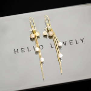 Detail view of long gold tassel earrings with pearls and crystals on reflective surface