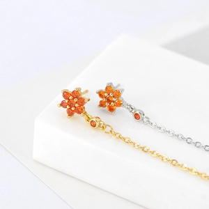 Detail of flower stud earrings with orange zircon and long tassel chains in gold and silver