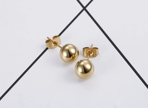 Macro shot of minimalist gold ball stud earrings with butterfly backings on texture
