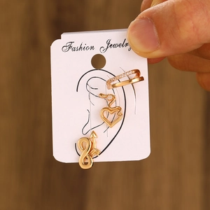 Detailed close-up of gold ear piercing set featuring heart, arrow, and crystal hoops
