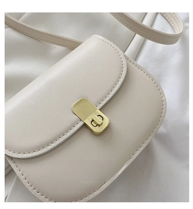 Detailed macro view of cream leather saddle bag with gold striped metal twist lock