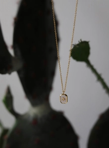 Detailed close-up of 18K gold starburst pendant with white shell inlay and tiny crystal